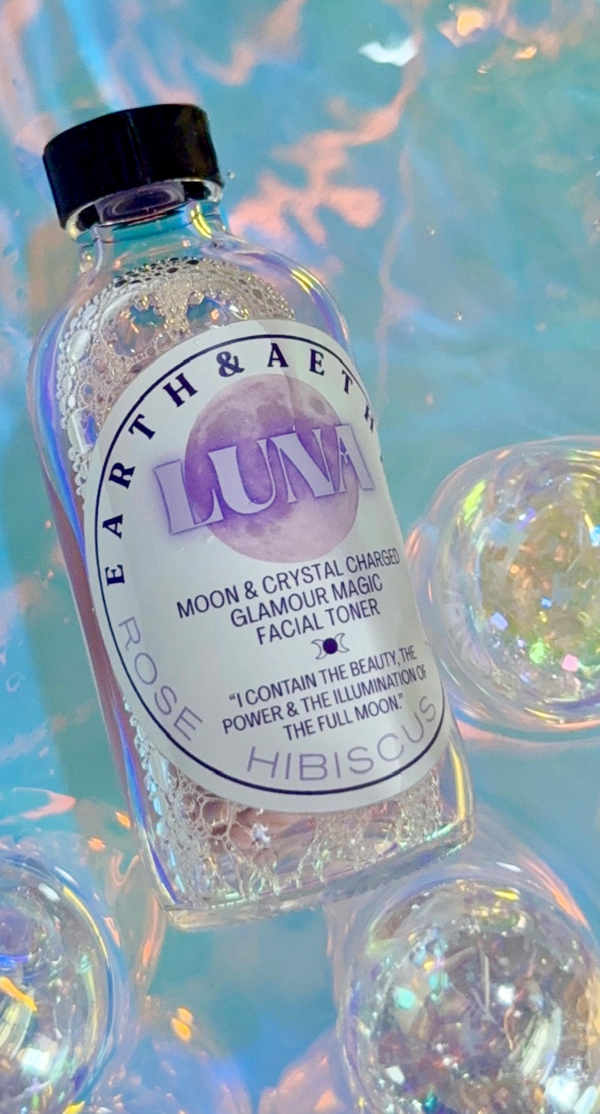 A bottle of Luna rose hibiscus facial toner resting on iridescent glass orbs
